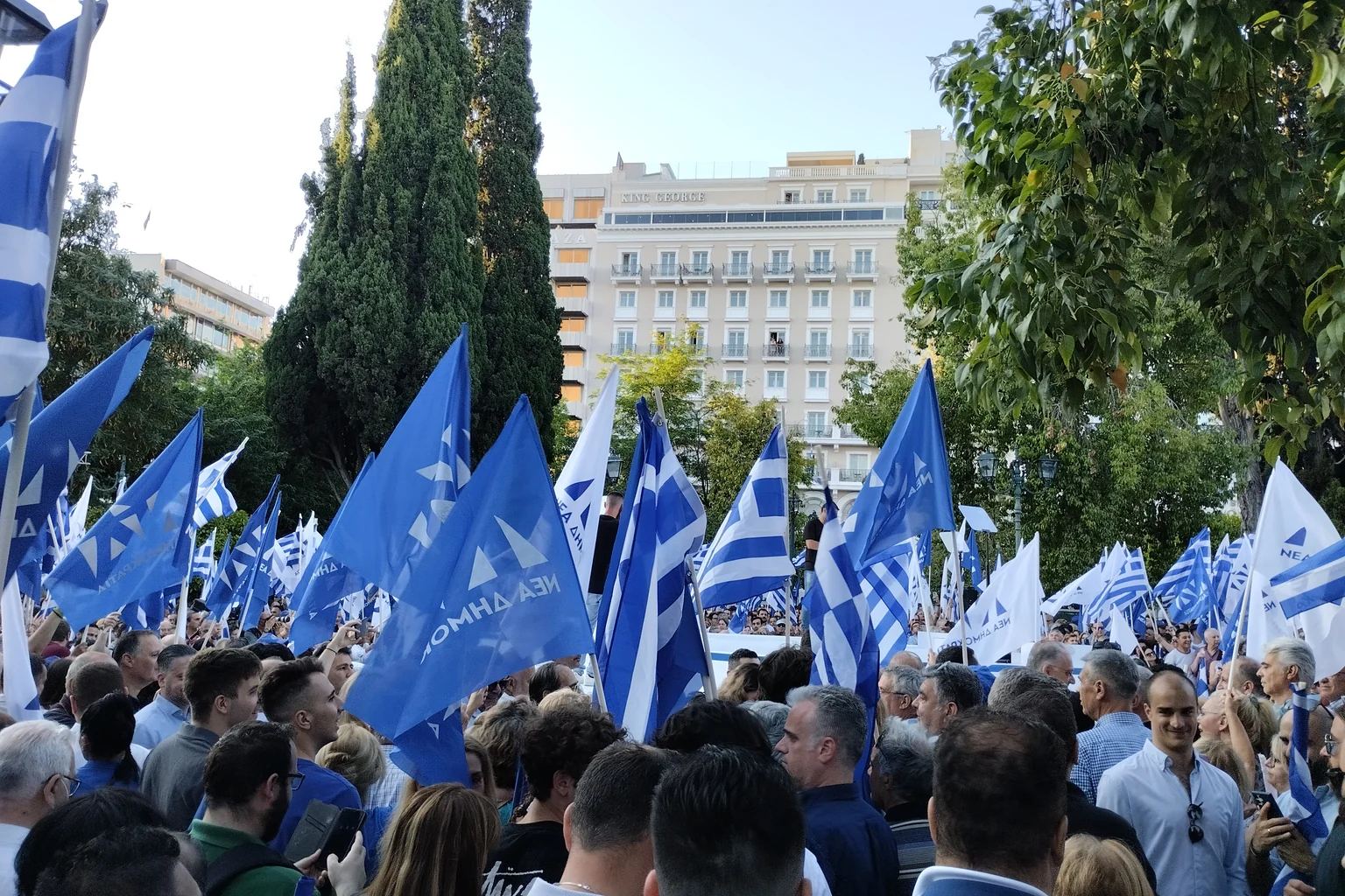 Πλήθος και μπλε-λευκές σημαίες της Νέας Δημοκρατίας μπροστά από δέντρα και κτίρια στο Σύνταγμα, σε φωτογραφία αρχείου του Ιουνίου 2023· όχι η επετειακή εκδήλωση του 2026.