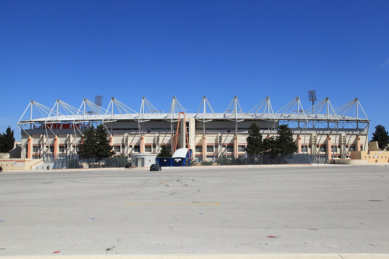 Εξωτερική άποψη του National Stadium στο Ta’ Qali, με κερκίδες, μεταλλικά στηρίγματα οροφής και σχεδόν άδειο χώρο στάθμευσης, σε φωτογραφία αρχείου.