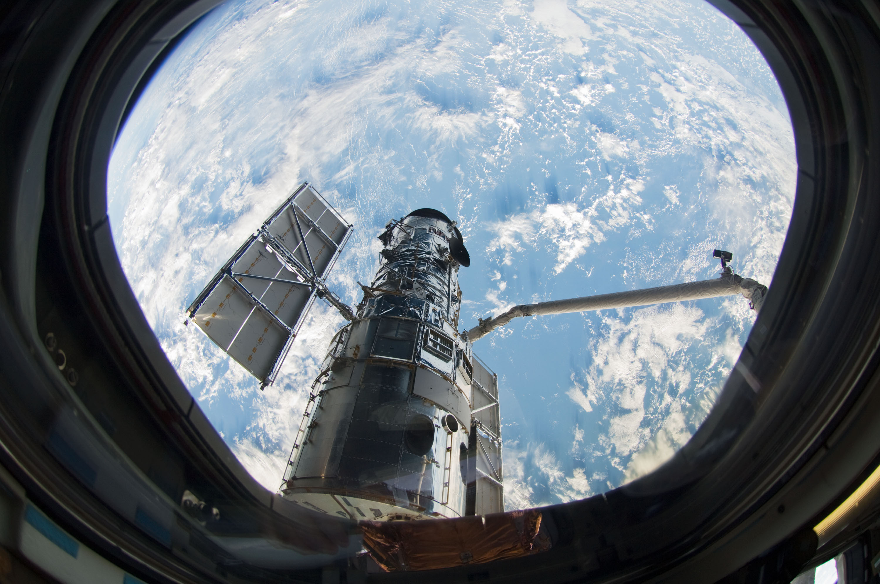 Το Hubble και τα ηλιακά του πάνελ πάνω από τη Γη, μέσα από κυκλικό παράθυρο του Atlantis, σε φωτογραφία αρχείου της 13ης Μαΐου 2009.