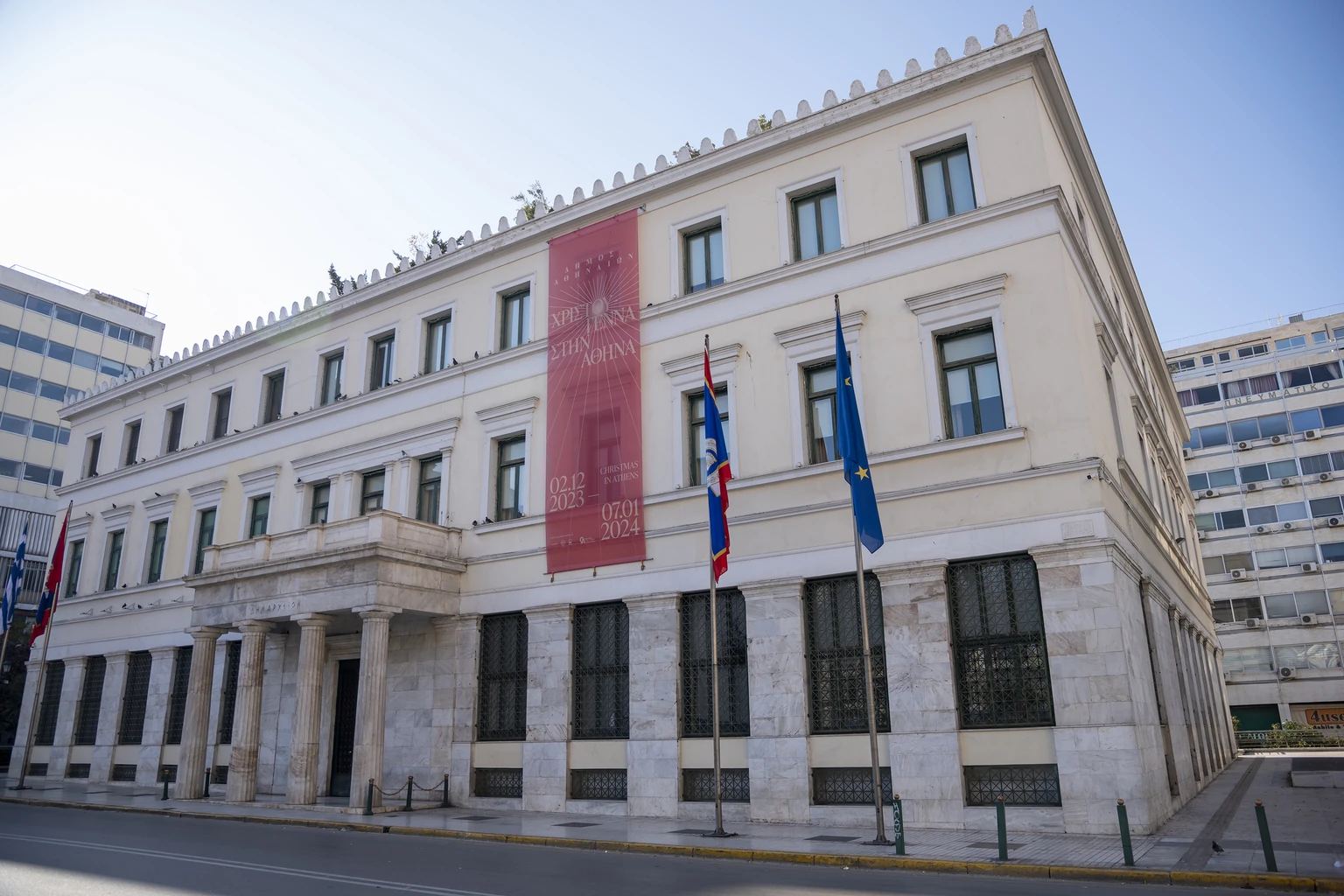 Το Δημαρχείο Αθηνών στην πλατεία Κοτζιά, με σημαίες και ιστορική αφίσα Χριστουγέννων 2023–2024, σε φωτογραφία αρχείου της 1ης Ιανουαρίου 2024· όχι η οικονομική ανασκόπηση του 2026.