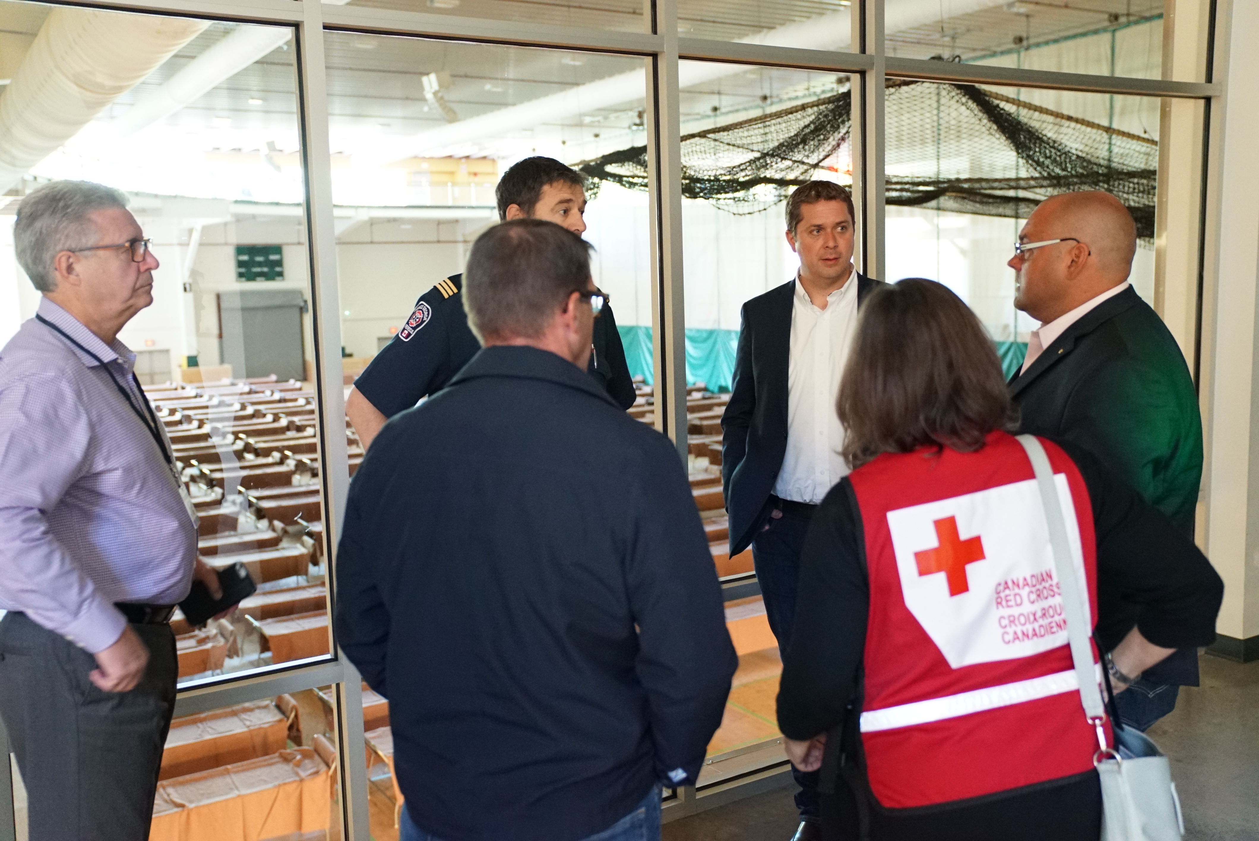 Ενήλικοι συζητούν δίπλα σε κλίνες κέντρου εκκένωσης· διακρίνεται γιλέκο του Καναδικού Ερυθρού Σταυρού. Φωτογραφία αρχείου του 2017.