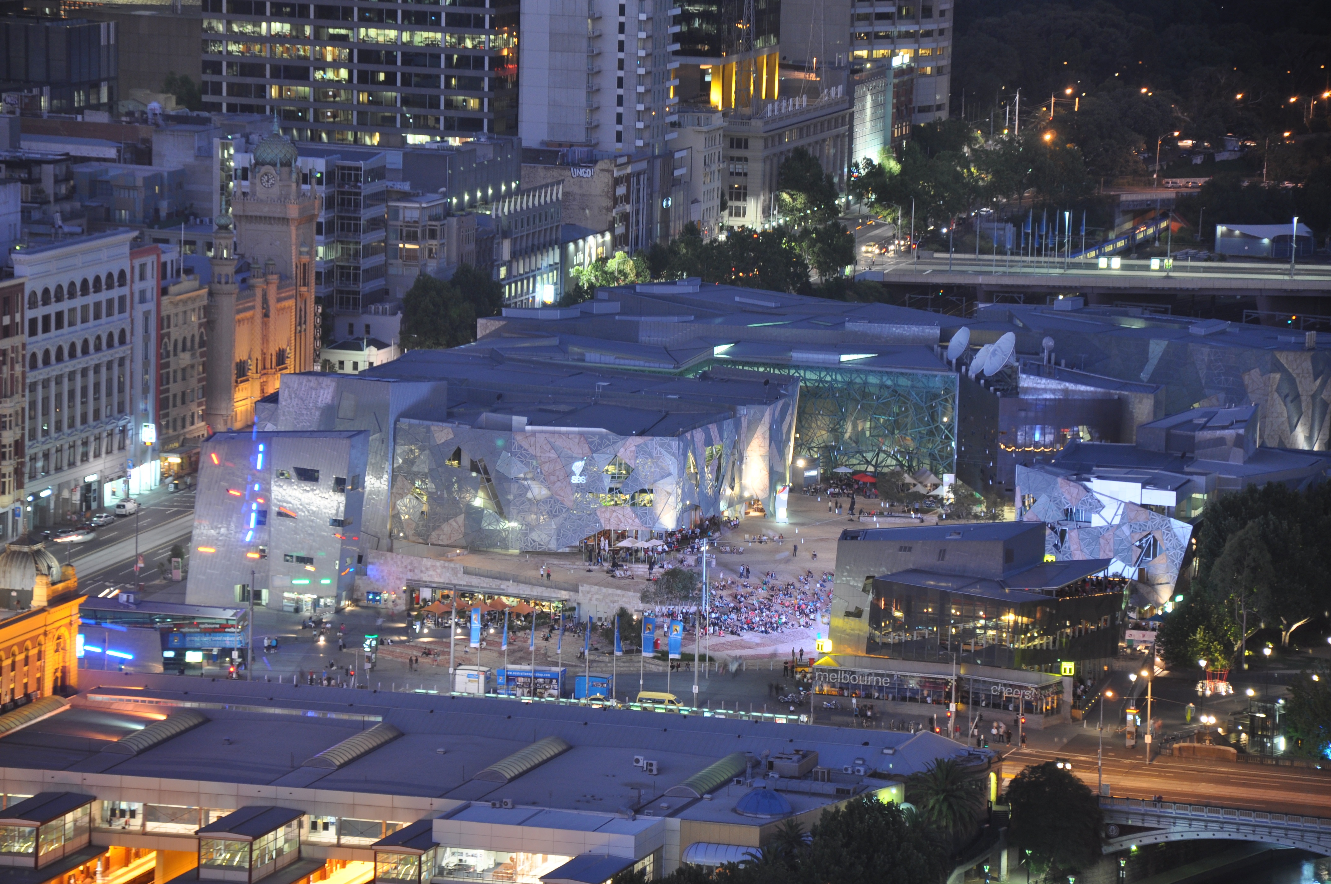 Η Federation Square στη Μελβούρνη με φωτισμένα κτίρια και μακρινό πλήθος. Φωτογραφία αρχείου, 21 Ιανουαρίου 2011· όχι εμφάνιση BIGYUKI το 2026.