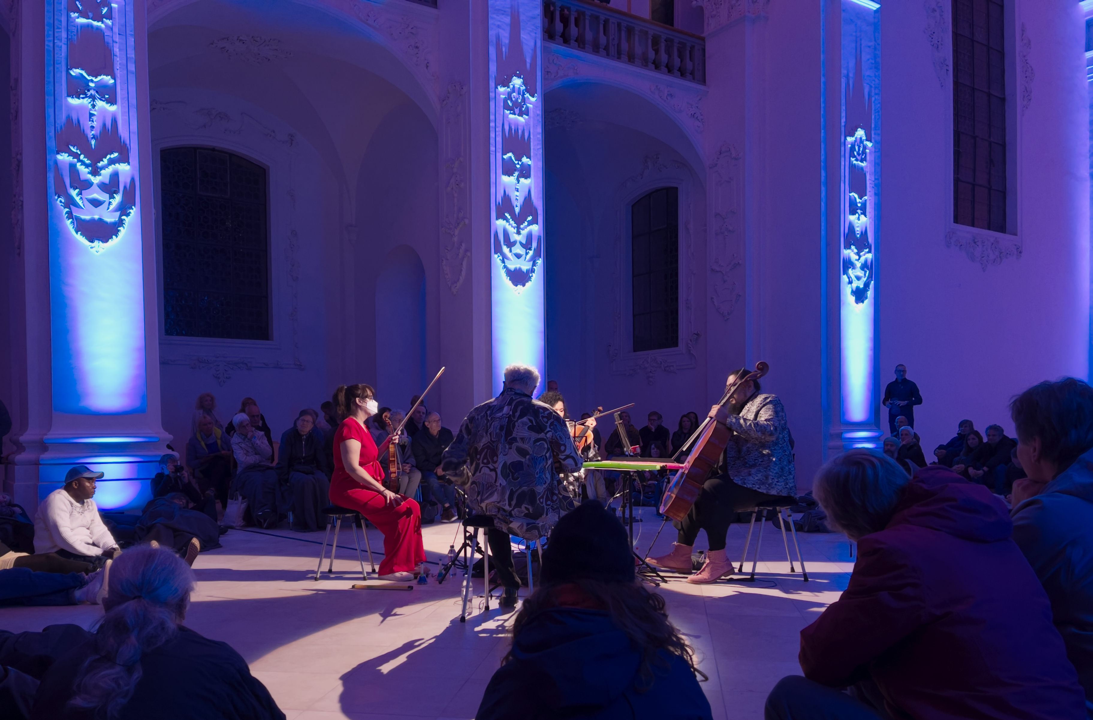 Το Kronos Quartet παίζει με έγχορδα σε ιστορική αίθουσα με μπλε φωτισμό και καθιστό κοινό· αρχείο του 2025.