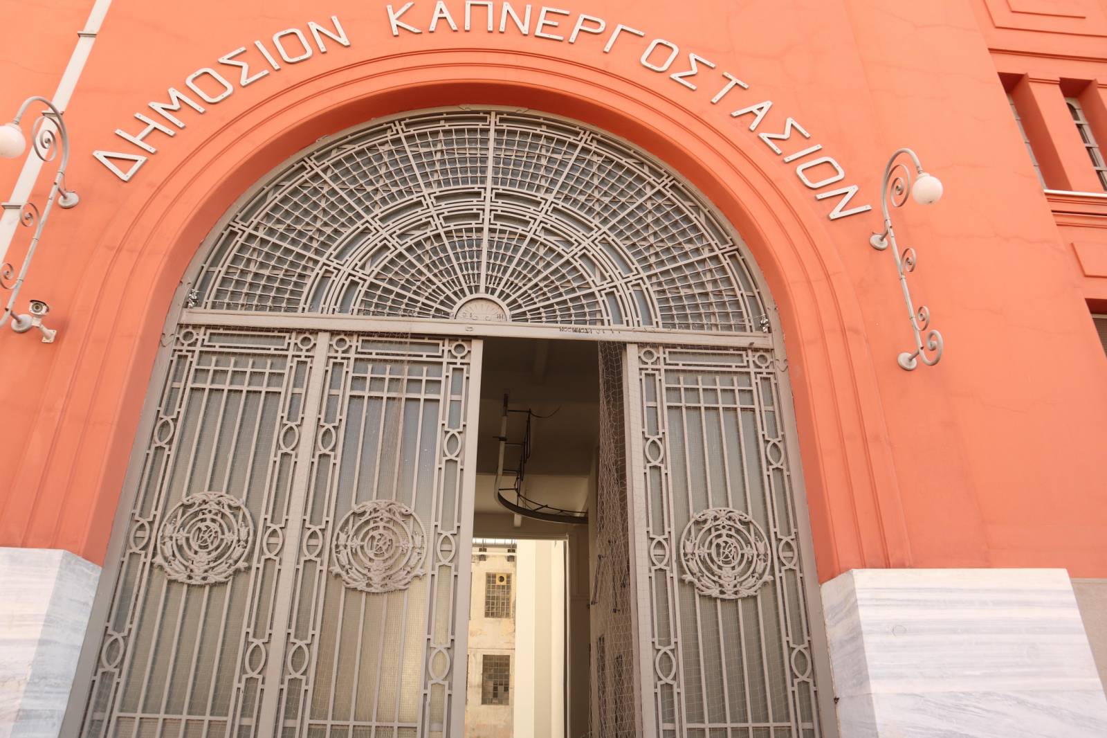 Αρχειακή φωτογραφία της πορτοκαλί εισόδου του Δημοσίου Καπνεργοστασίου με αψιδωτή μεταλλική πόρτα και την επιγραφή του κτιρίου· όχι η έκθεση του 2026.